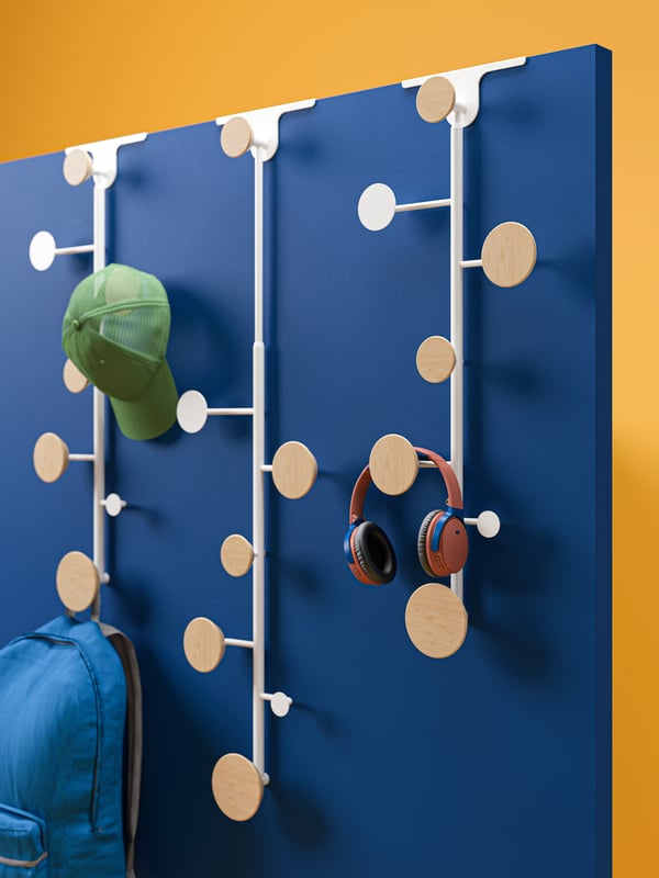 Several BÄRFIS hooks with a rucksack, headphones and cap hang on a dark blue wall against a yellow background.