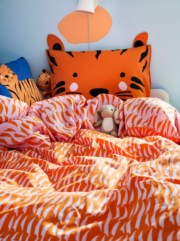 Close-up of NATTHÄGER duvet cover and pillowcase with orange tiger, a little DVÄRGHARE soft toy rabbit chilling in bed.