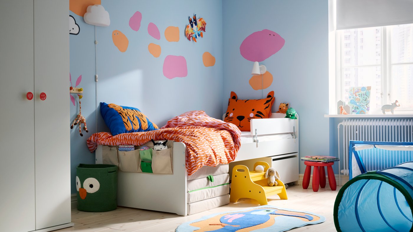 A children’s room with lots of colours, a SLÄKT bed along the light blue wall with pink and orange dots painted on it.