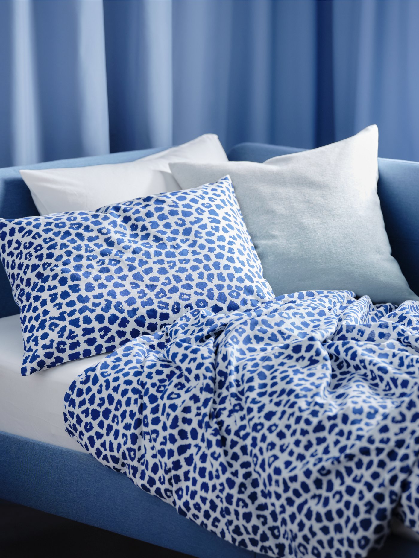 Una struttura letto imbottita blu con copripiumino e federe KVASTFIBBLA con motivo leopardato bianco/blu scuro - IKEA