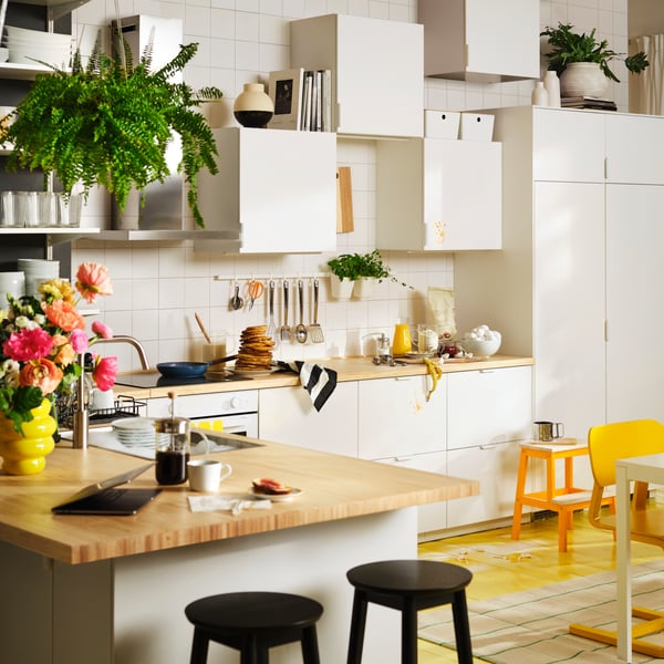A lively kitchen with white appliances, base cabinets with wooden worktops, and wall cabinets with white VEDDINGE doors.