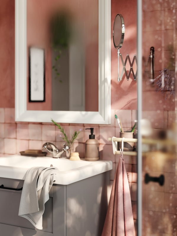 A pink bathroom features a grey ENHET base cabinet with a white washbasin and a white mirror above it and towels on the side.