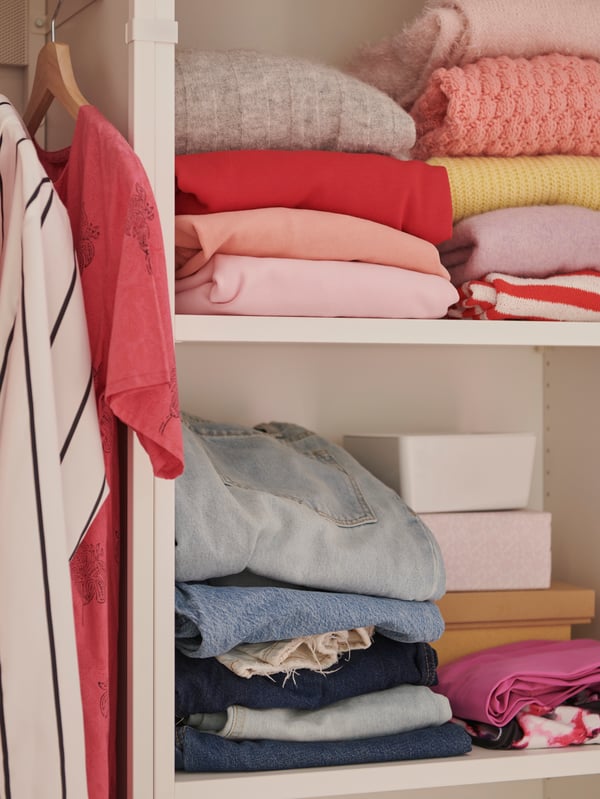Gros plan sur la tringle et les tablettes d’une armoire-penderie PLATSA avec des vêtements suspendus sur des cintres BUMERANG et pliés sur les tablettes.