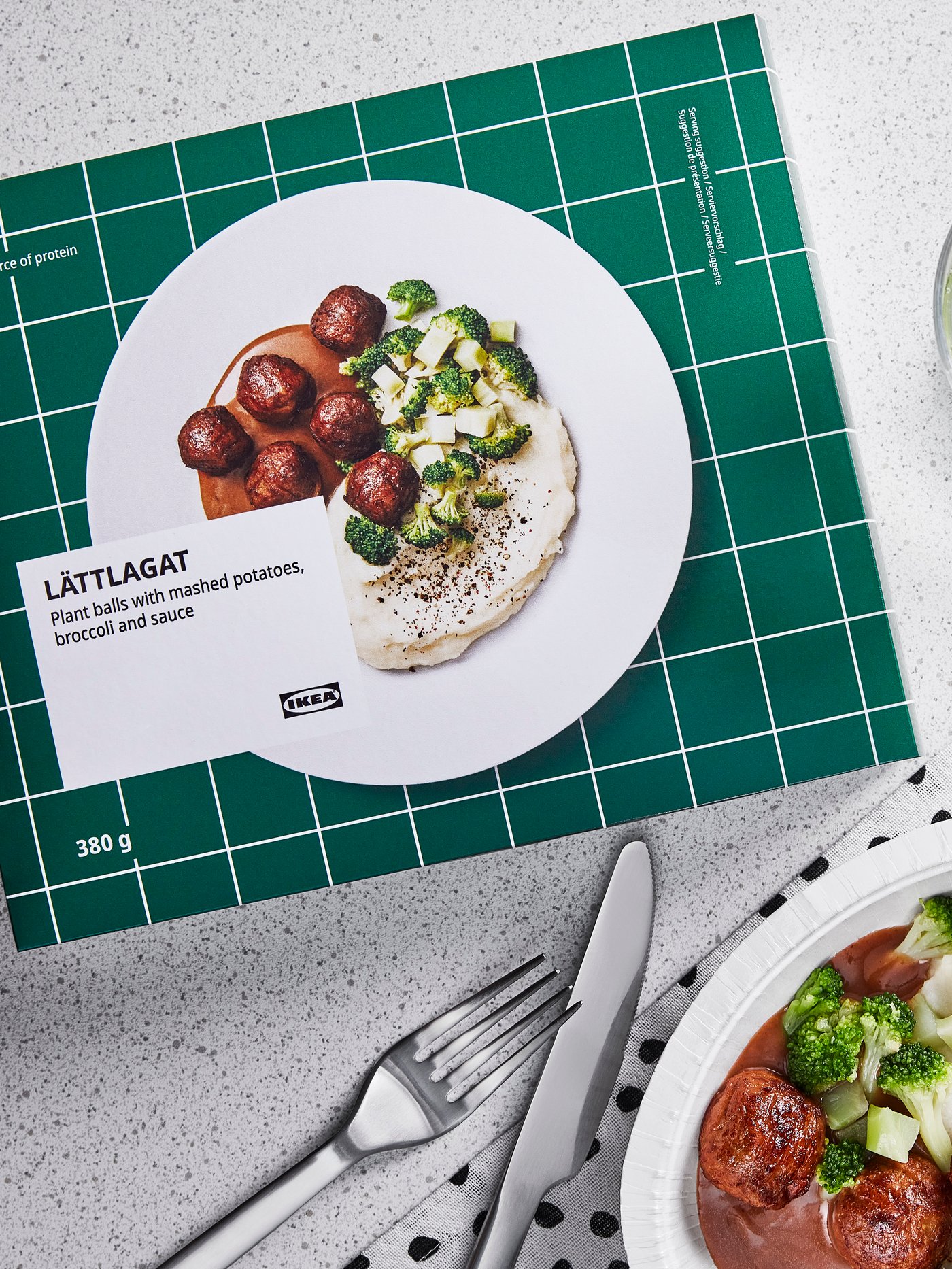 A LÄTTLAGAT ready meal packet next to a plate containing the prepared meal on a white, speckled table.