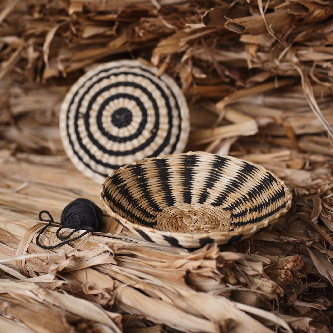 The MÄVINN wall decoration set of 2 and a roll of black cotton string sit on a pile of beige banana bark material.