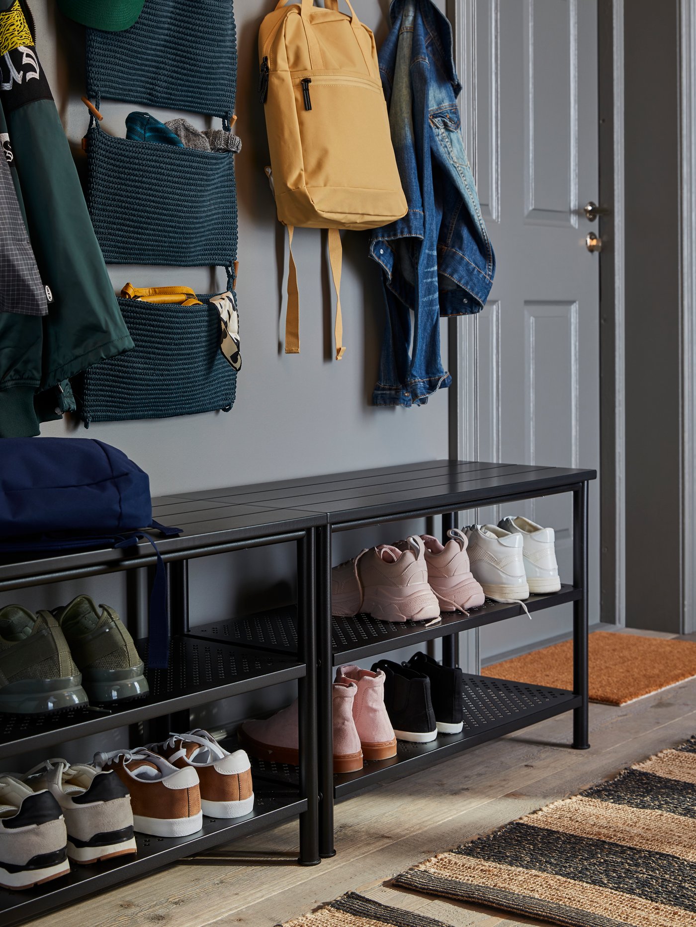 Two PINNIG benches with shoe storage holding shoes and boots stand in a hallway. NORDRANA hanging storage hangs above.