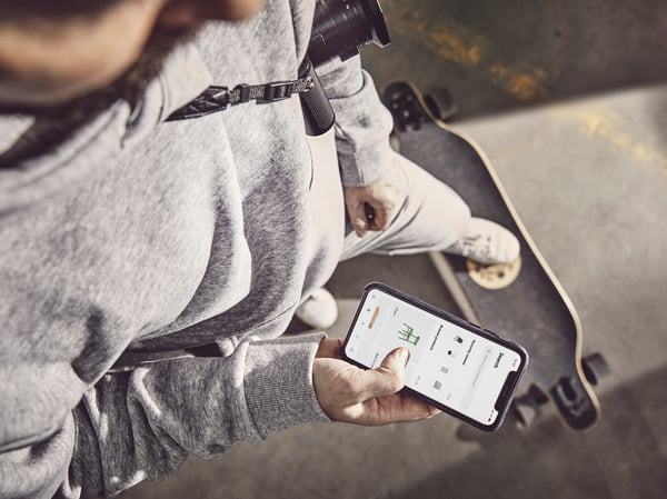 A person seen from above on a skateboard, holding a smartphone displaying the IKEA app.