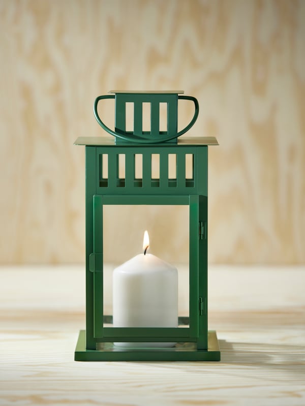 A green BORRBY lantern with a lit candle inside is sitting in a space with wooden walls and floors.
