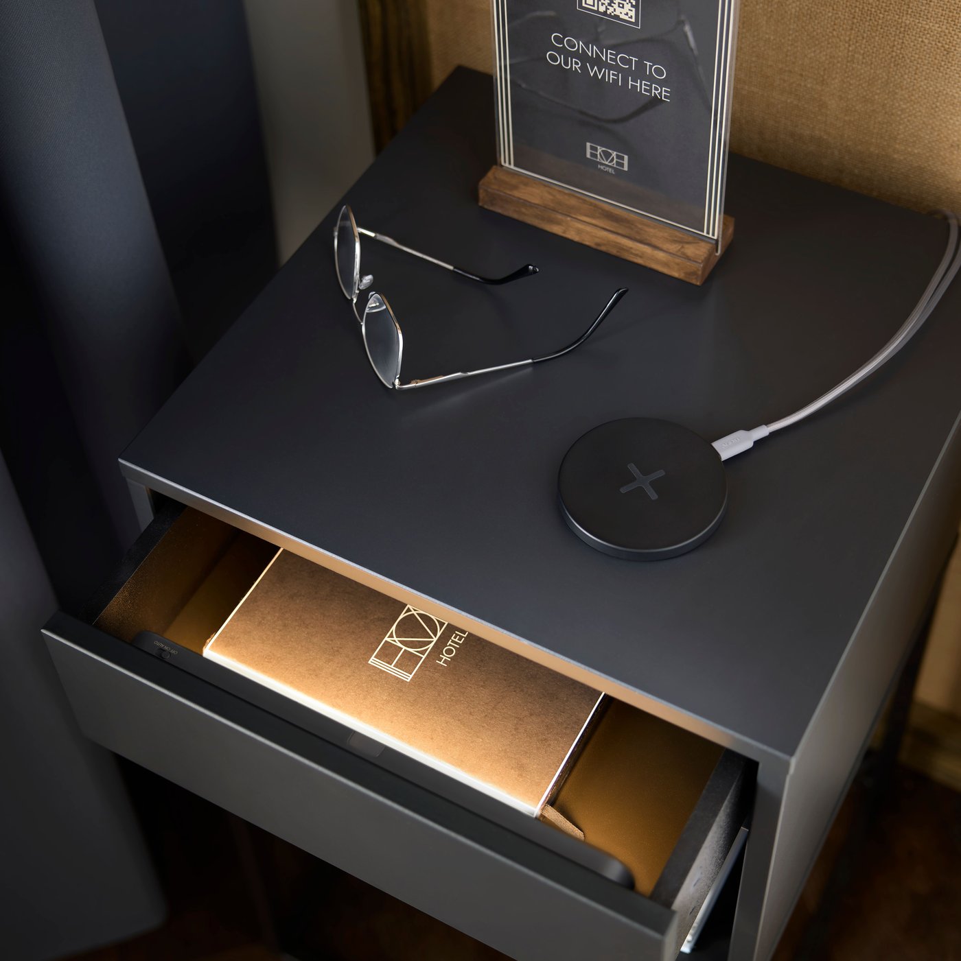 Eine leicht geöffnete Schublade eines Ablagetisches, der in einem Hotelzimmer steht, wird von einer superschlanken, batteriebetriebenen KÖLVATTEN LED-Beleuchtung mit Sensor sanft beleuchtet.
