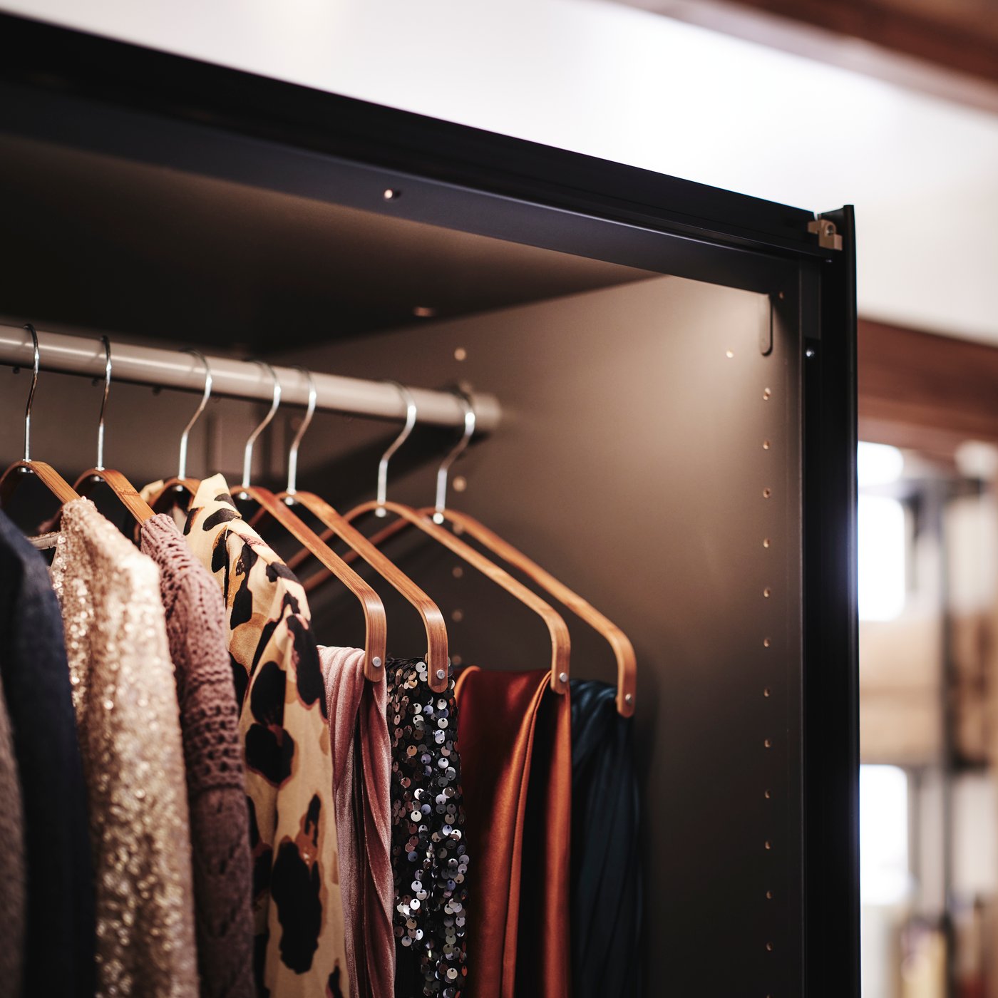 Close-up of PAX MEHAMN wardrobe with one of the sliding doors opened to show integrated lighting and clothes hanging inside.