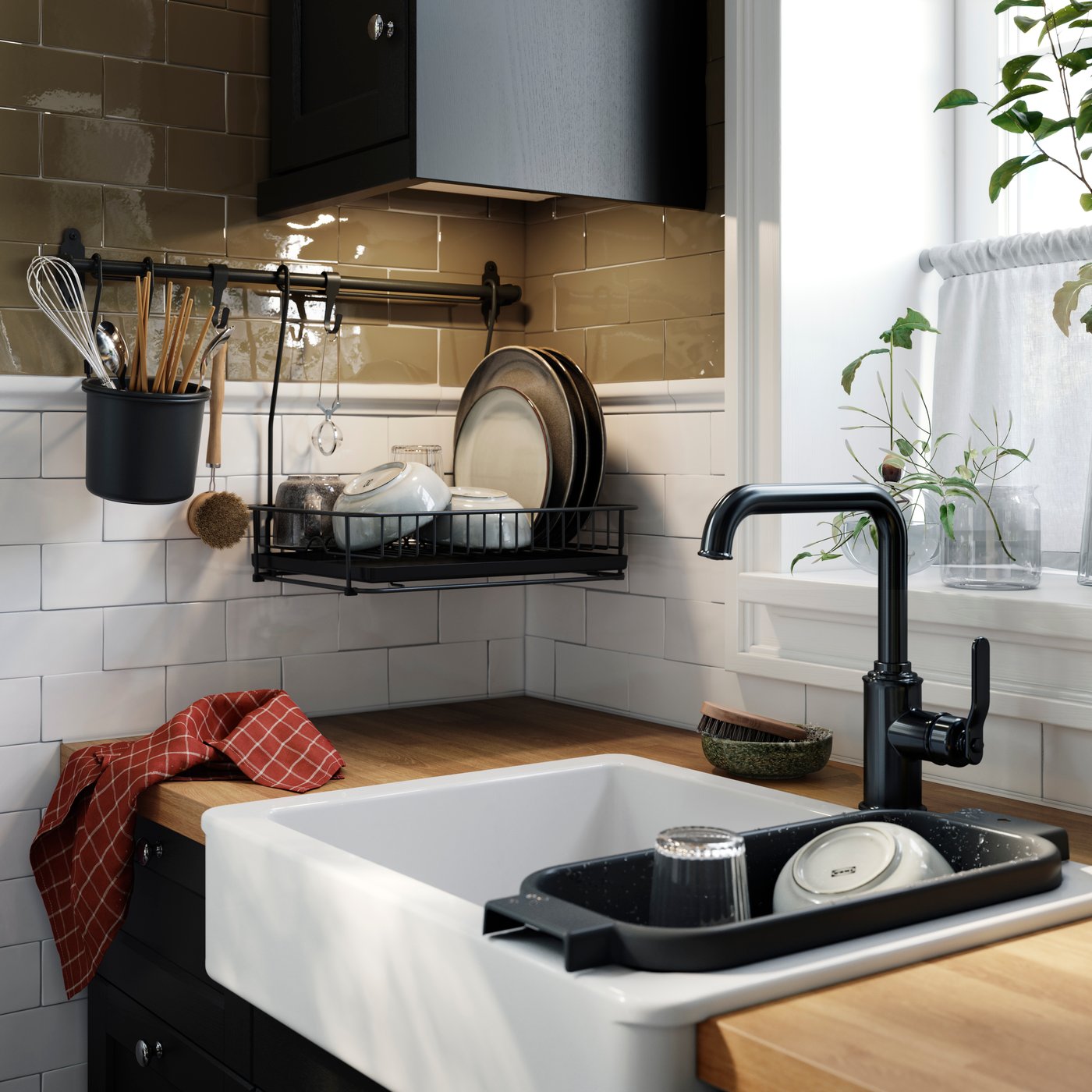 A kitchen with a black HULTARP rail holding dishes and utensils, above a wooden worktop with a sink and plants.