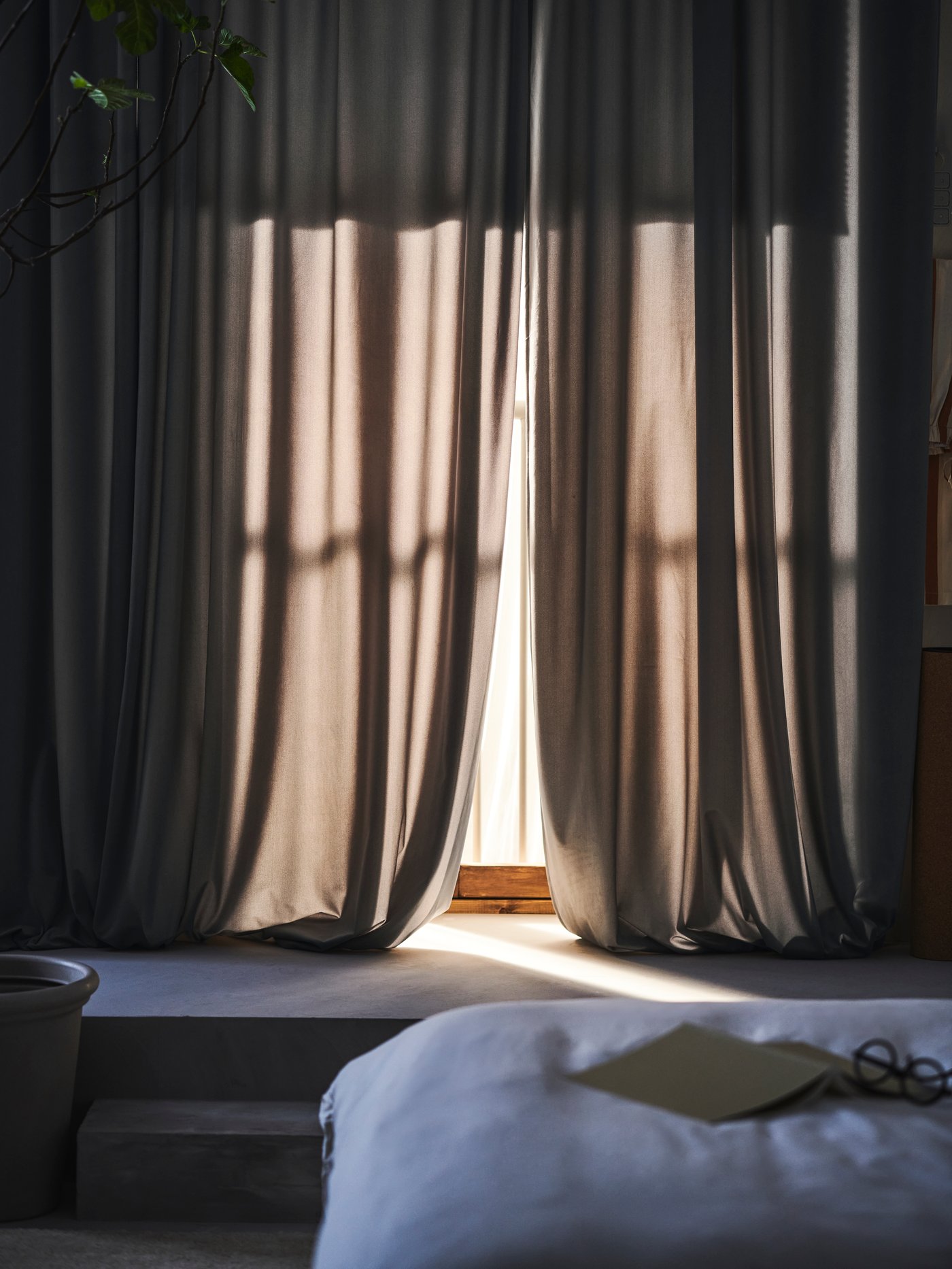 The sun shines on a pair of grey‑white SANDSVINGEL curtains in the bedroom.