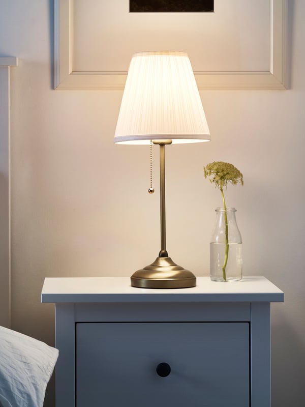 A brass/white ÅRSTID table lamp in the bedroom