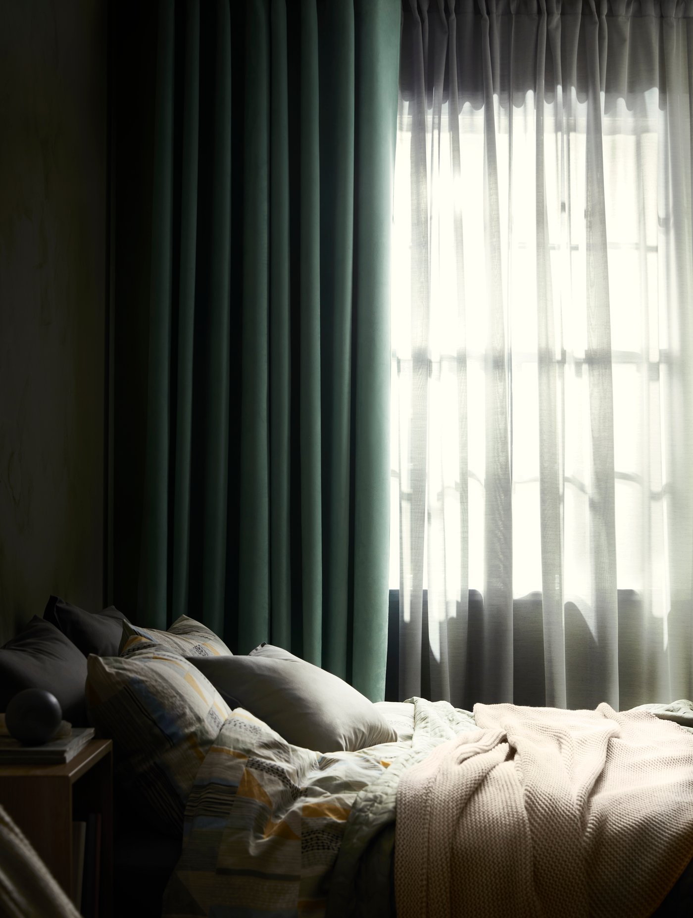 Cortina BIRTNA verde enn un dormitorio al costado de una cama. Tapando la ventana un velo HILJA.