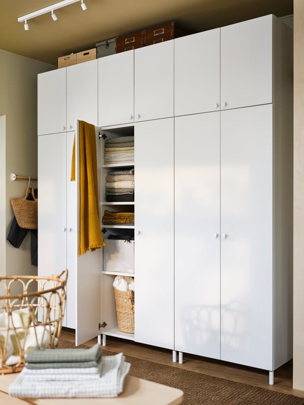Armoire-penderie PLATSA blanche à douze portes, avec une serviette de bain jaune suspendue à une porte ouverte, montrant le linge de lit à l’intérieur.