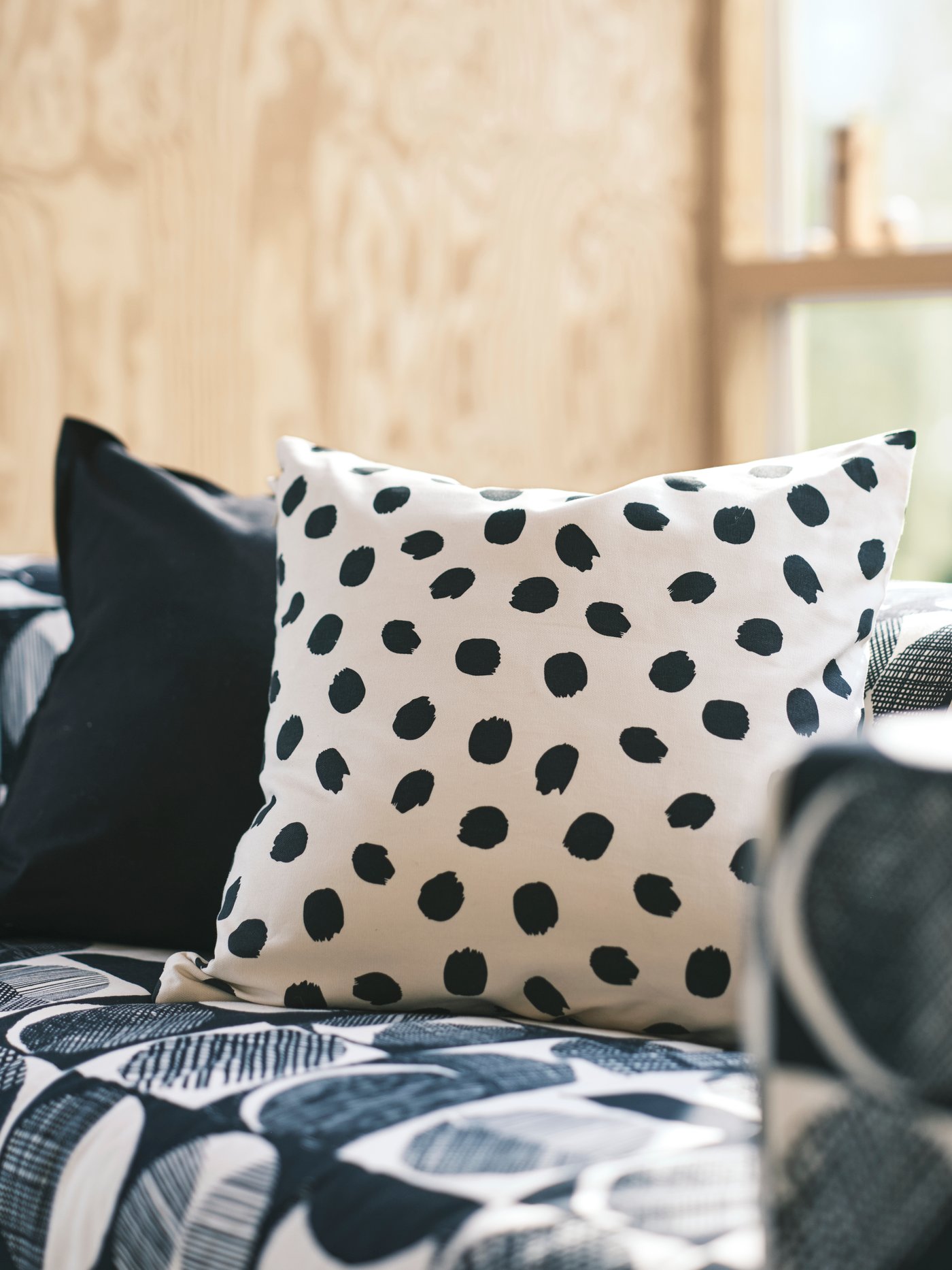 Sofa KLIPPAN berwarna hitam/kuning air di ruang berwarna neutral dengan kusyen di dalam sarung kusyen GURLI berwarna hitam dan ODDNY corak bintik terletak di atasnya.