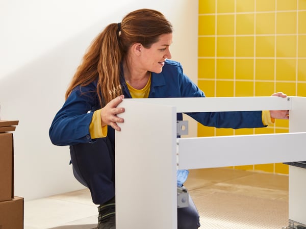 Un employé d'IKEA est à genoux sur le sol de la salle de bain, tenant un WC blanc.