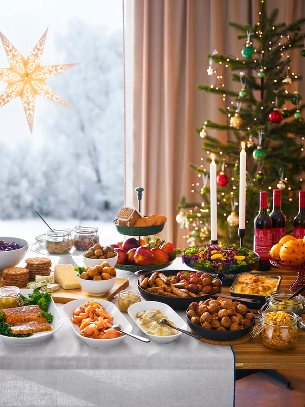 A table set with a selection of various Christmas foods such as meatballs, herring, salmon and bottles of mulled wine called glögg.