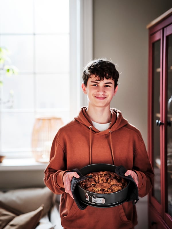 A person in a kitchen using grey RINNIG pot holders to hold a freshly baked tart in a grey HEMMABAK springform pan.