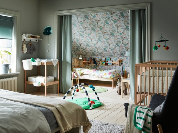 Cozy children's room with a bed, crib and play area. Floral wallpaper, soft tones and practical storage solutions create a warm atmosphere.