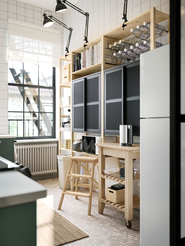 A pine IVAR shelving unit with two black mesh cabinets with doors and dark grey work lamps up top, plus a kitchen cart.