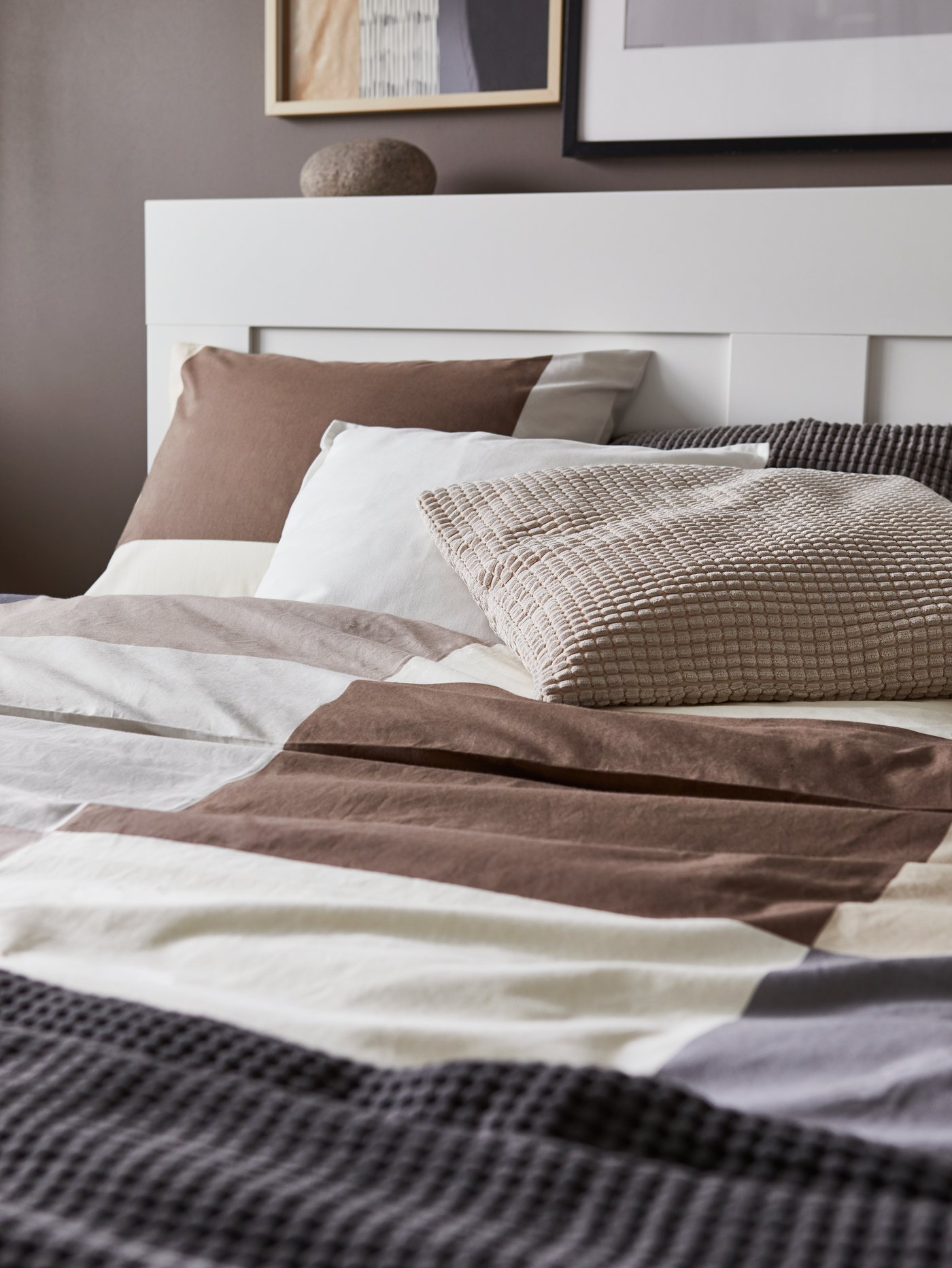 Katil berwarna putih dengan kepala katil, sarung kuilt dan sarung bantal bercorak warna coklat, alas berwarna kelabu dan kusyen berwarna putih, kelabu dan kuning air.