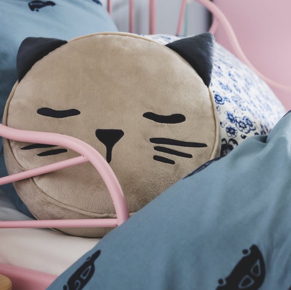 A beige BARNDRÖM cushion with pocket and a cat’s face and ears lies on a MINNEN extendable bed with BARNDRÖM bed linen.