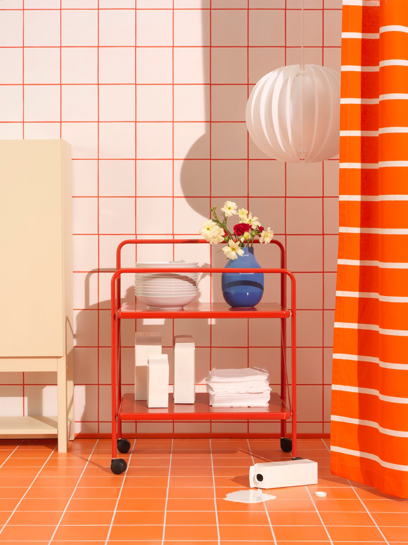 Različni izdelki podjetja IKEA pred steno z belimi ploščicami in oranžnimi podrobnostmi, kjer so celo tla povsem oranžna.