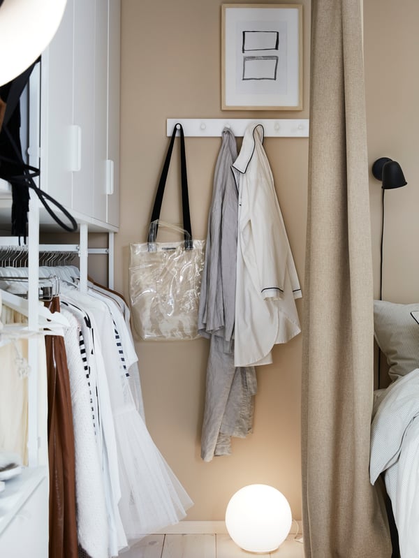 Vêtements aérés sur patère LURT/GUBBARP en blanc à six boutons, fixée au mur près d’une penderie ouverte.