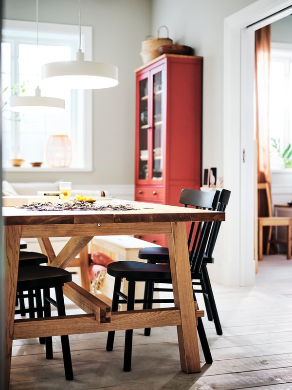 Deux suspensions NYMÅNE blanches allumées au-dessus d’une table MÖCKELBY en chêne autour de laquelle sont disposées des chaises NORRARYD noires.
