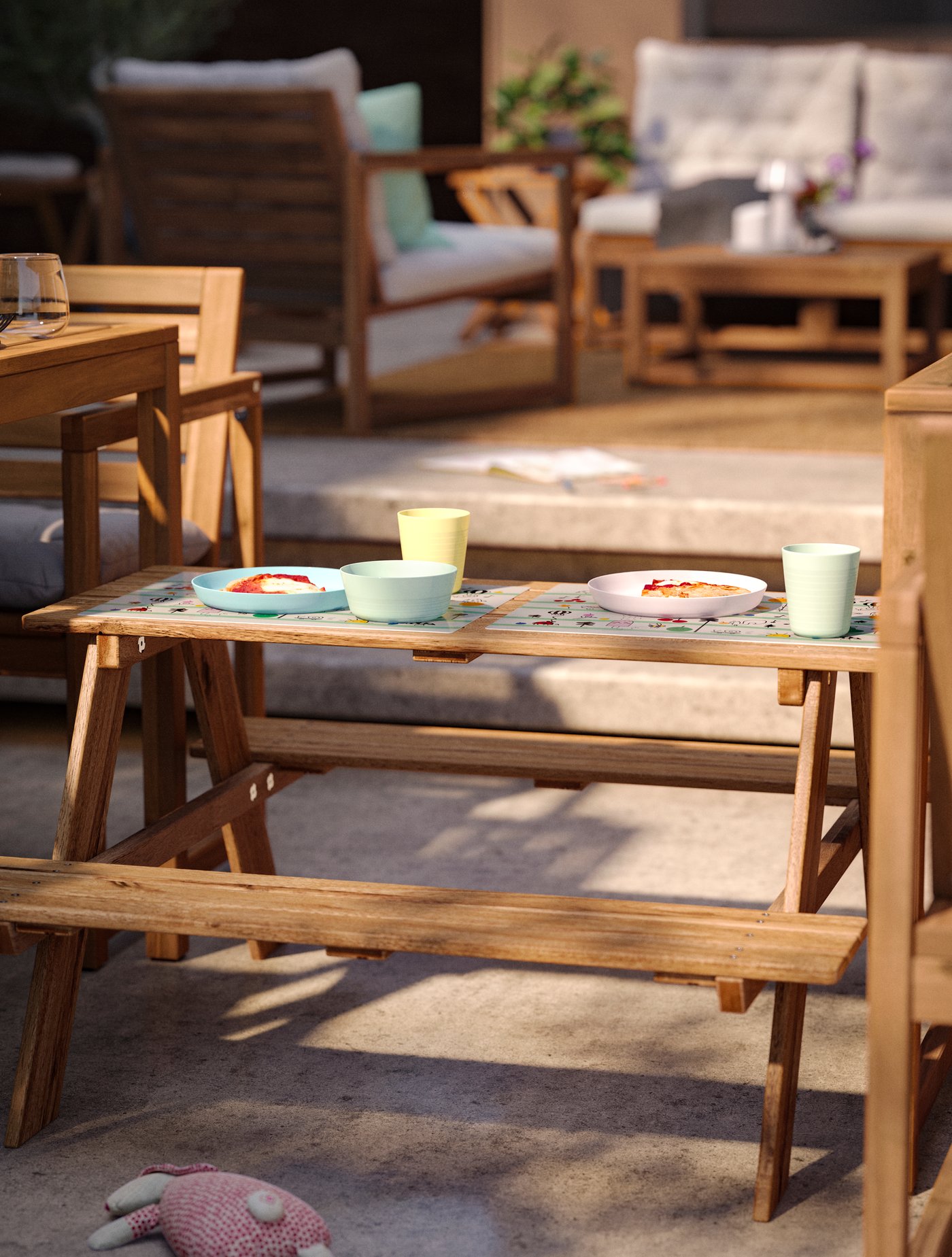 Área de comedor exterior soleada con dos mesas y una mesa de picnic infantil RESÖ, decorada con platos y tazas en colores pastel.