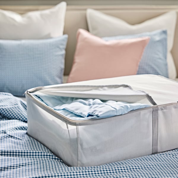 A HEMMAFIXARE storage base, containing bed textiles, is placed on a neatly made bed with a blue and while duvet cover.