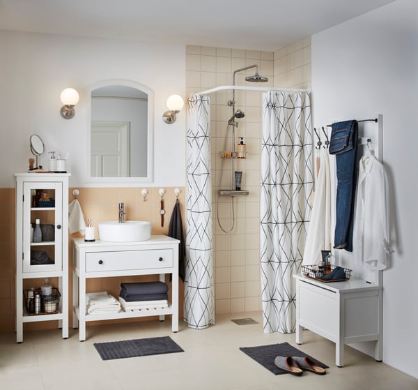 A white HEMNES wall shelf holding bottles, makeup and a white towel on a black metal rack attached to the shelf.