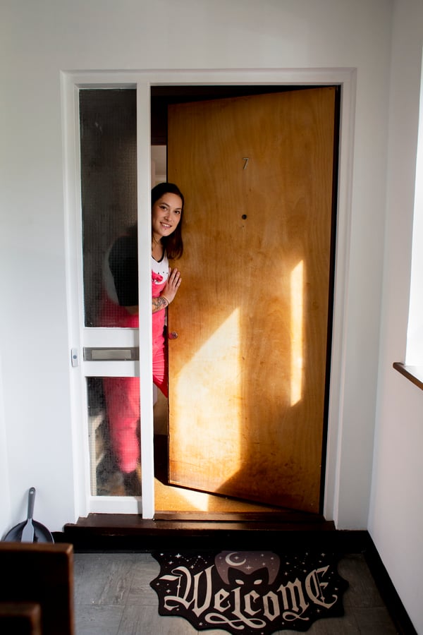 Woman opening her front door and smiling, looking out, with a welcome mat on the floor below the door.