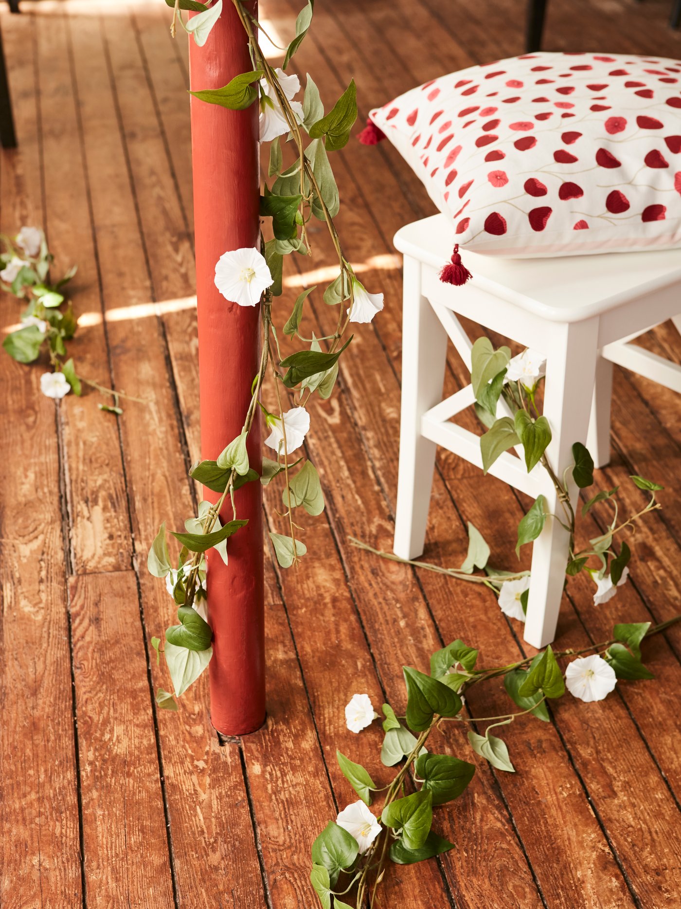 An ANLEDNING artificial garland with white flowers and green leaves hanging on a pillar indoors and across a white chair.
