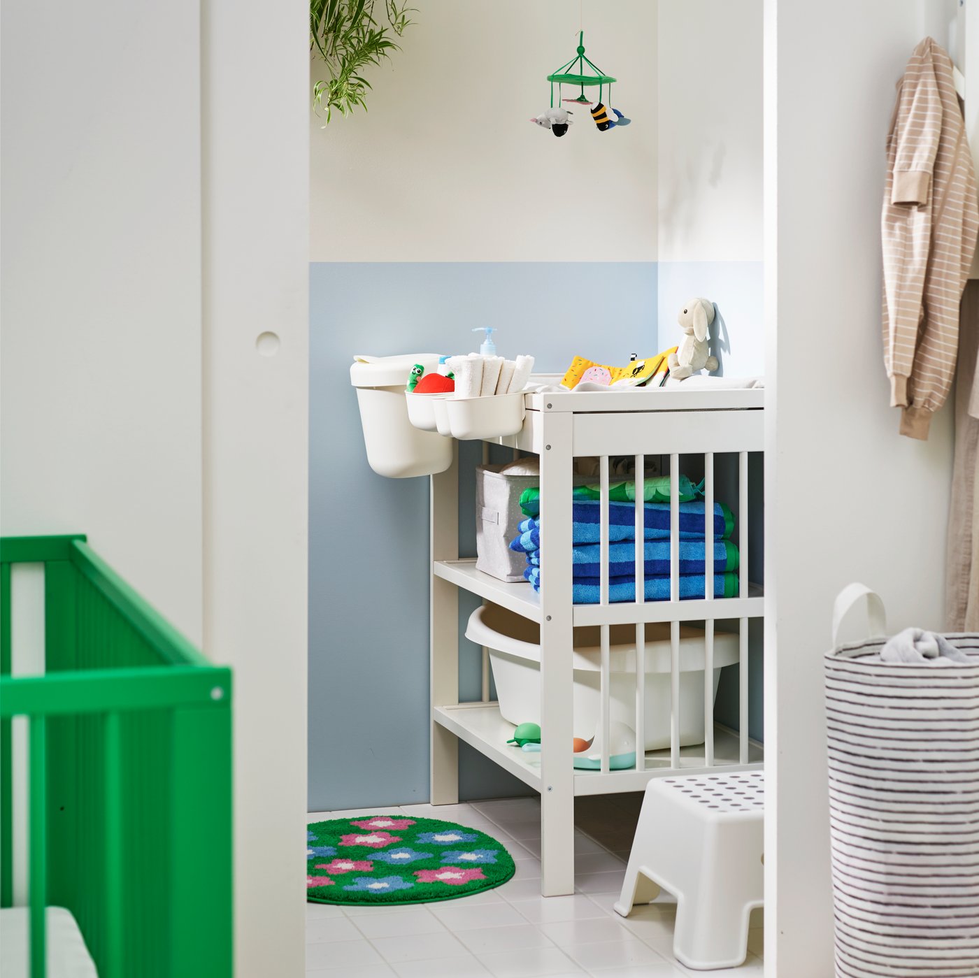 Ett ljust barnrum med ett vitt GULLIVER skötbord, prydligt organiserat med babyartiklar och färgglada handdukar.