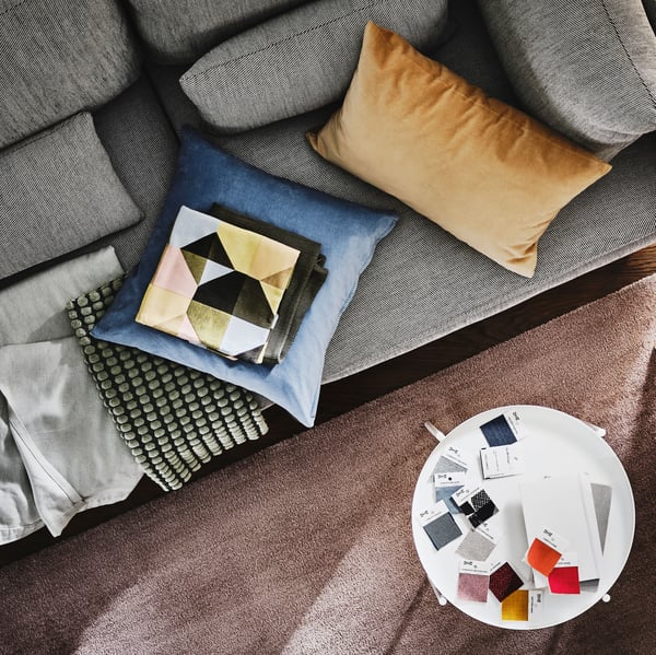 A SÖDERHAMN 3-seat sofa with colourful cushions on it stands beside a side table with colour swatches on it.