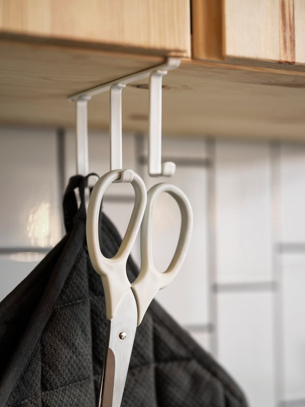 A PÅLYCKE clip-on hook rack attached to a cabinet, holding a white pair of scissors and two grey pot holders.