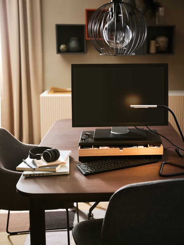 An ELLOVEN monitor stand holding a monitor on top, with the drawer open and a keyboard half underneath, on top of a table.