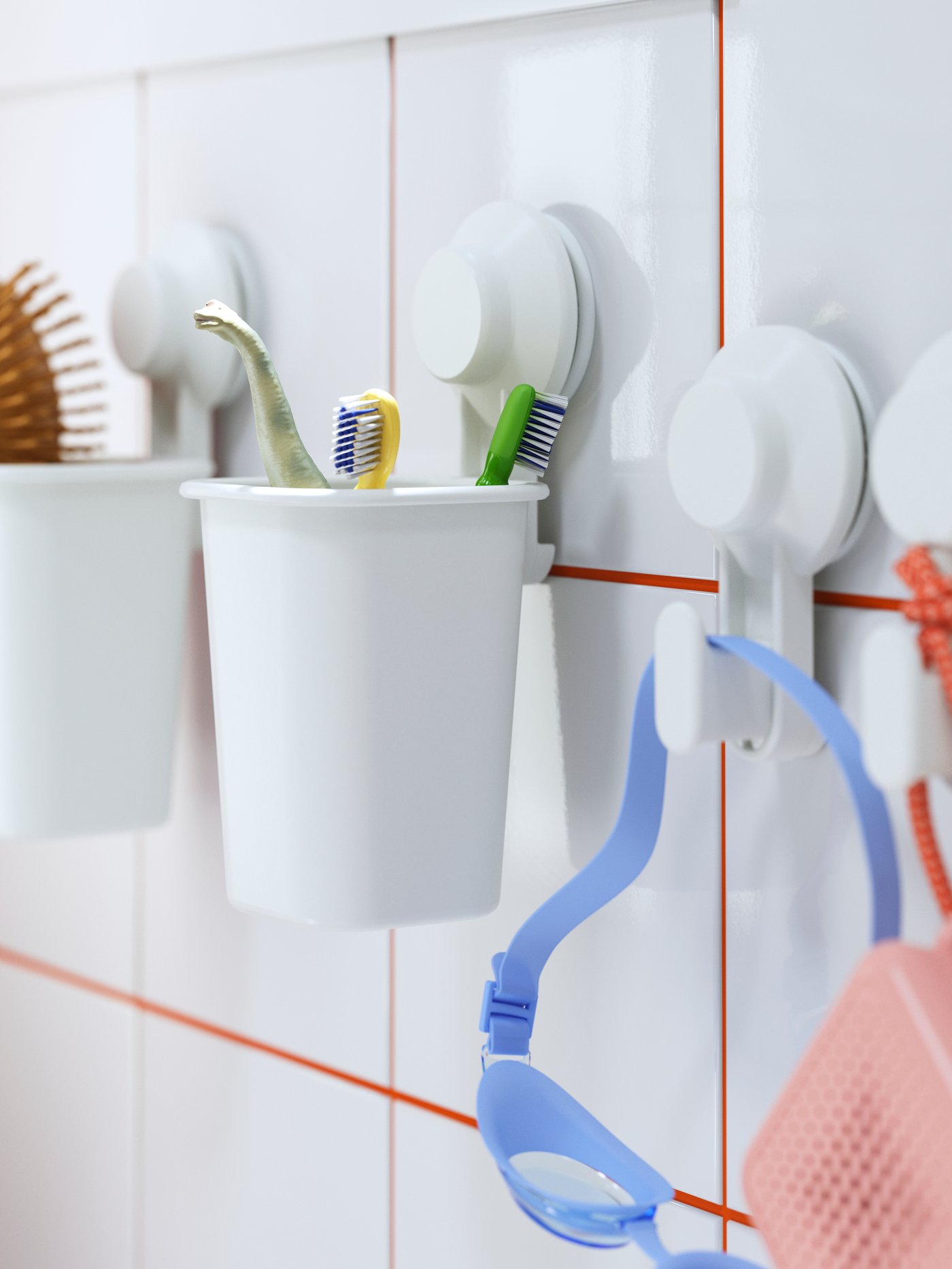 A TISKEN toothbrush holder with suction cups holding toothbrushes and a hairbrush, with goggles hanging beside it.