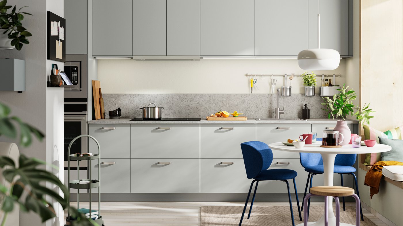 HAVSTORP light grey kitchen fronts with a grey worktop, blue chairs around a white dining table, and potted plants.