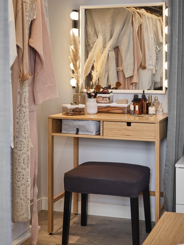 A beauty station where a bamboo NORDKISA dressing table and a SAKARIAS stool sit under a NISSEDAL mirror and two wall lamps.