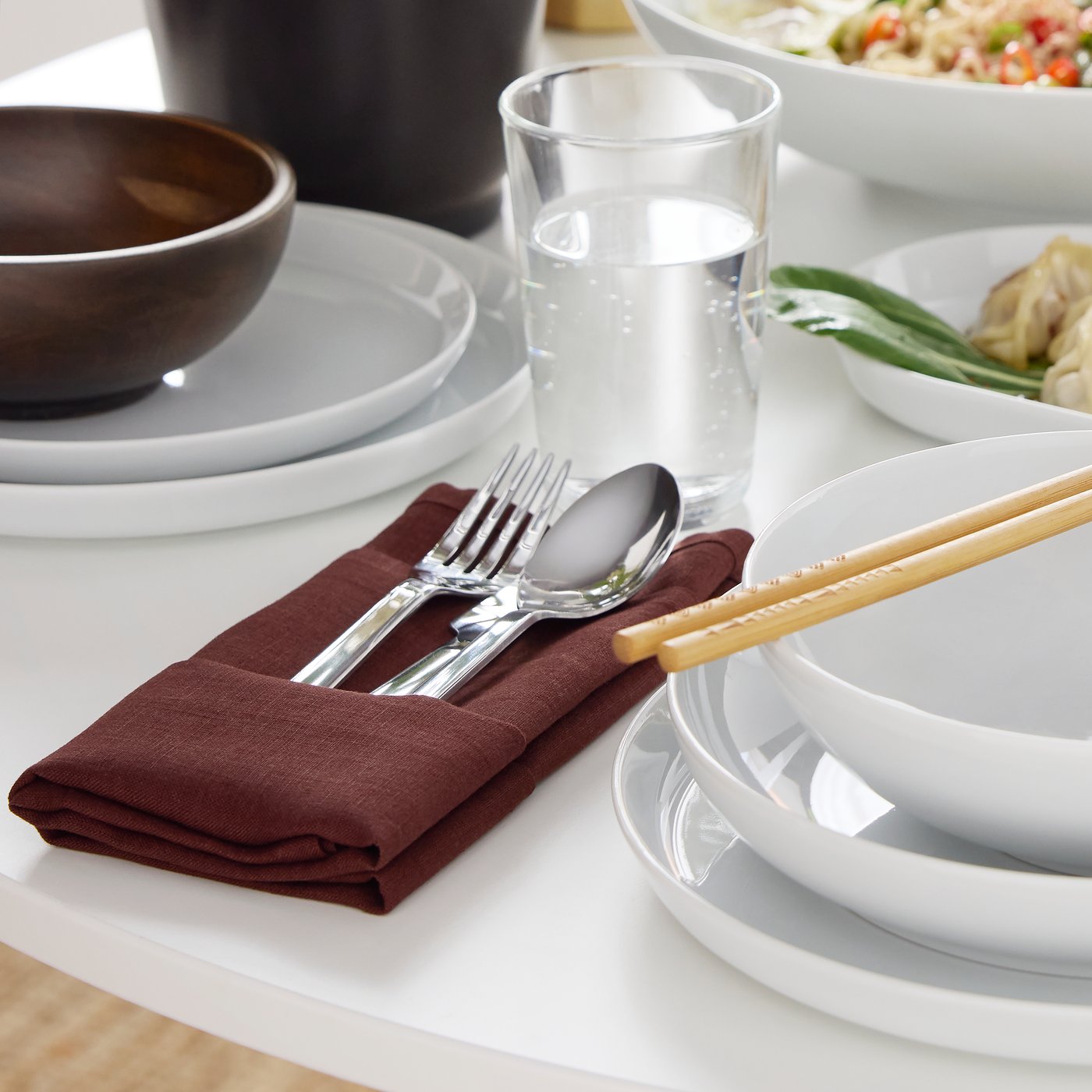 Una forchetta, un coltello e un cucchiaio della serie di posate IKEA 365+ sono appoggiati su un tovagliolo STOCKHOLM 2025 rosso scuro piegato.