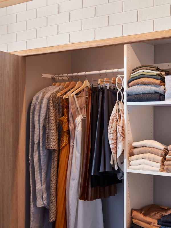 The inside of a fitted AURDAL wardrobe combination with some clothes hanging from rails and other clothes folded on shelves.
