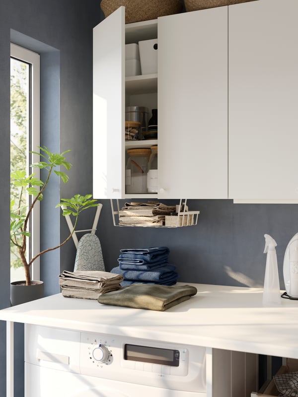 An ENHET storage combination with wall-mounted cabinets above a washing machine and a white worktop with folded clothes.