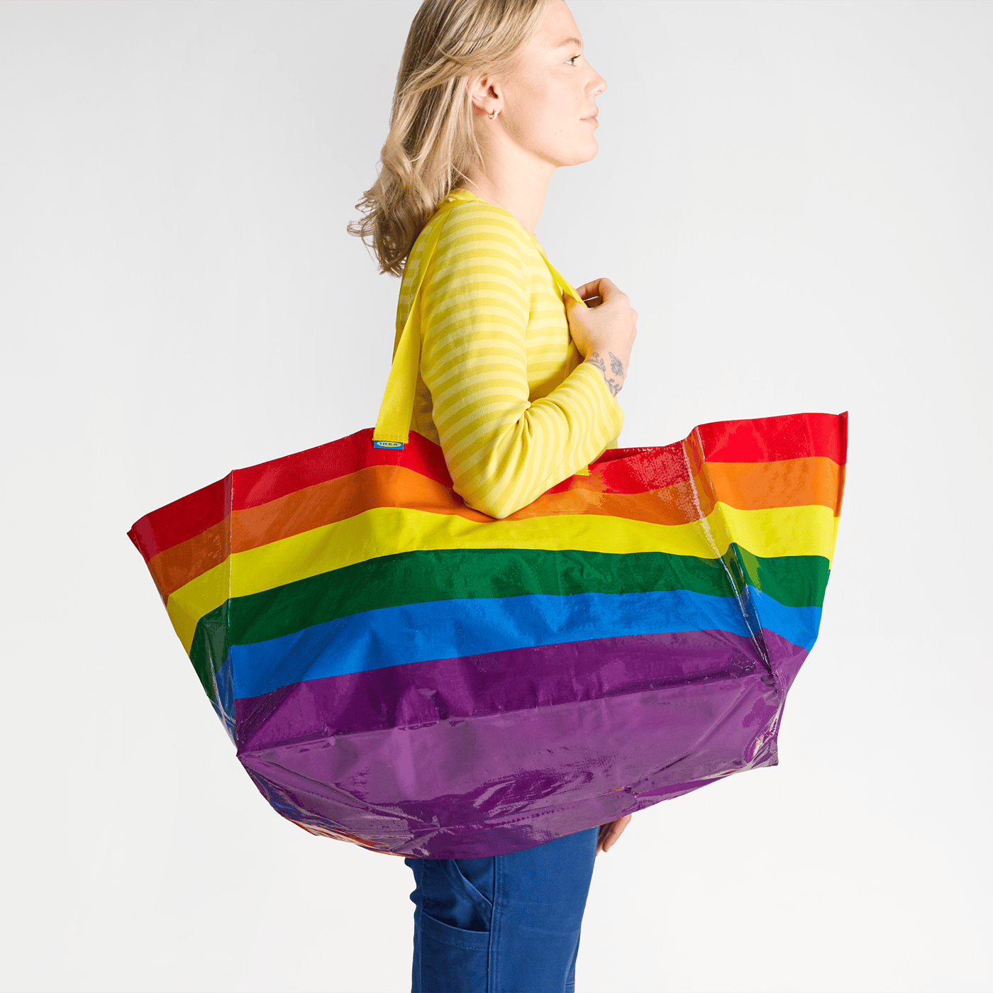 An IKEA co-worker wearing an IKEA uniform, holding a STORSTOMMA rainbow bag.