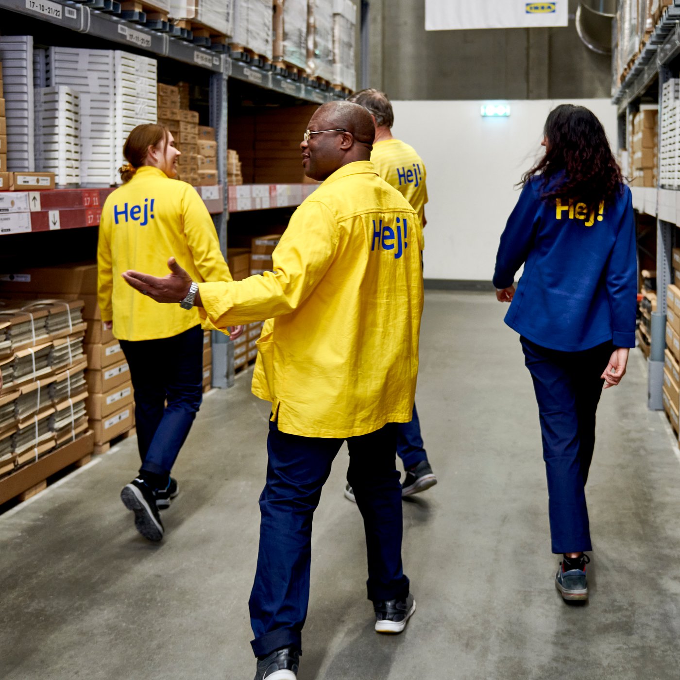 Een diverse groep van IKEA medewerkers wandelt door de zelfbedieningsafdeling van een IKEA winkel