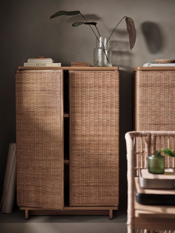 Two FRYKSÅS cabinets stand side by side in a living room, with one door slightly ajar and books and a plant on top.