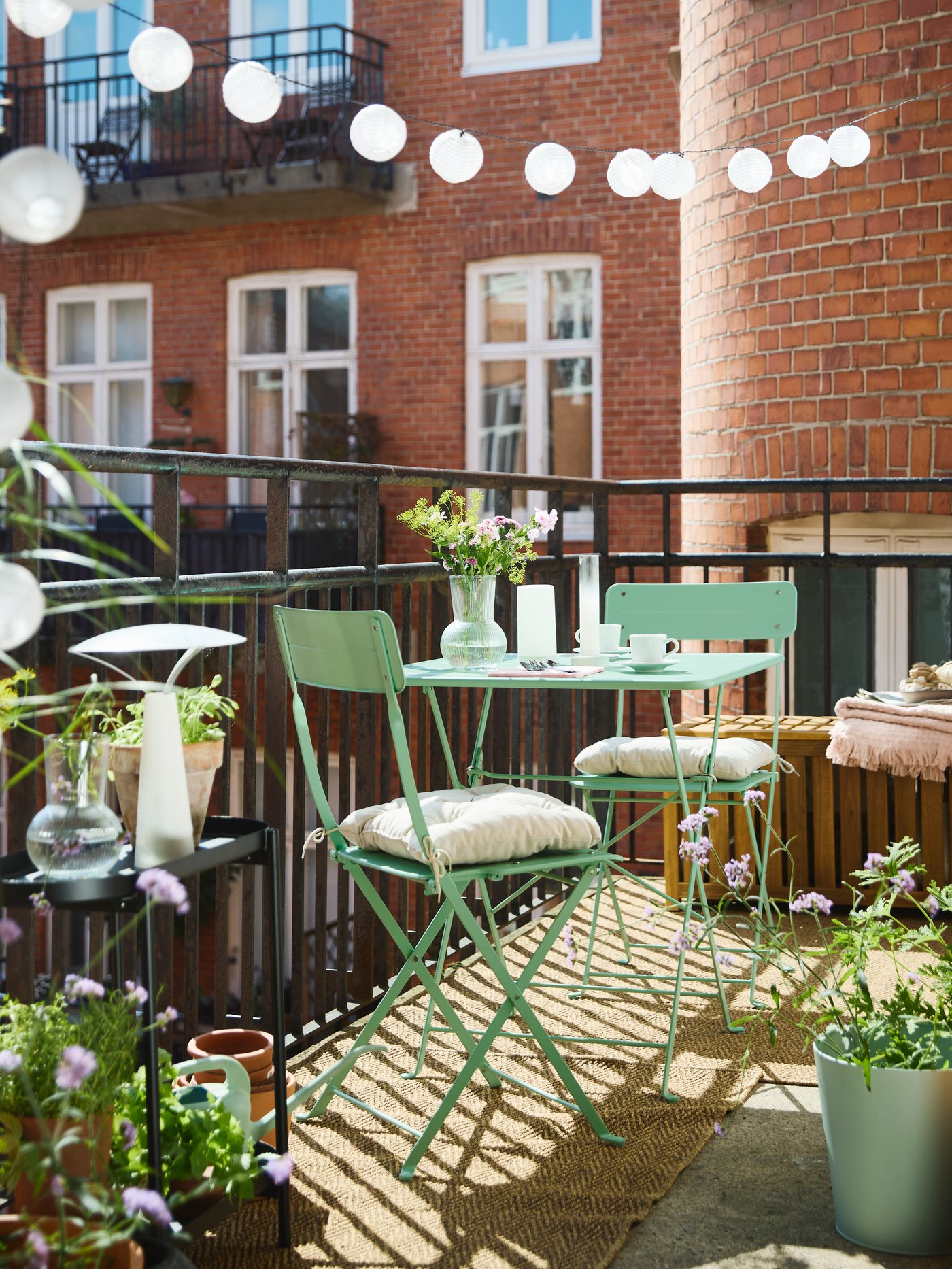 Small balcony in a romantic setting with SUNDSÖ bistro table for two in light green, KUDDARNA pillows and OLIVBLAD plant stand.