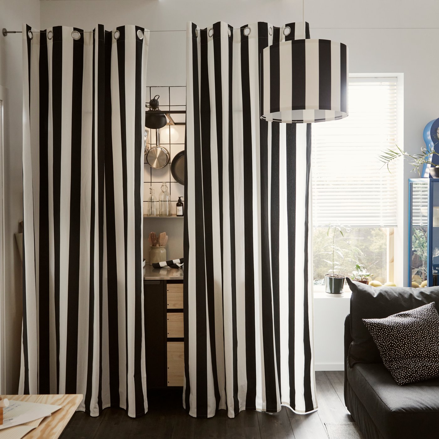 Black and white striped SLÅNHÖSTMAL curtains hanging around a kitchenette that is hinted, placed next to a tall window.